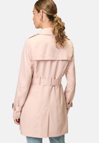 Light pink trench coat with a belted waist, wide collar, and long sleeves. Features a back pleat and button details on sleeves.