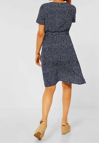 Vestito navy con motivo a pois bianchi, maniche corte, fascia elastica in vita e vestibilità ampia. Abbinate a sandali con zeppa color beige.