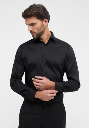 Camicia nera a maniche lunghe realizzata in tessuto morbido, dotata di colletto classico e chiusura frontale con bottoni, con bottoni abbinati e polsini aderenti.