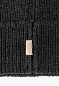 Berretto in maglia nera con una texture a coste e un orlo piegato. Presenta un piccolo tag bianco con testo arancione che dice "BLK." Il materiale sembra spesso e caldo.