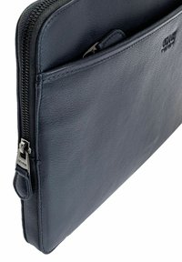 Skórzana osłona na laptopa w ciemnoniebieskim kolorze o teksturowanej powierzchni, z zamkiem błyskawicznym na górze i zewnętrzną kieszenią slip. Detale w kolorze srebrnym.