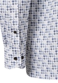 Witte blouse met blauwe en grijze bloemenpatronen, voorzien van zwarte knopen op de manchetten en een textuur van katoen.