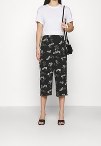 Culottes noirs à motif floral blanc, fabriquées en tissu léger. Associées à un t-shirt blanc court et des accessoires noirs.