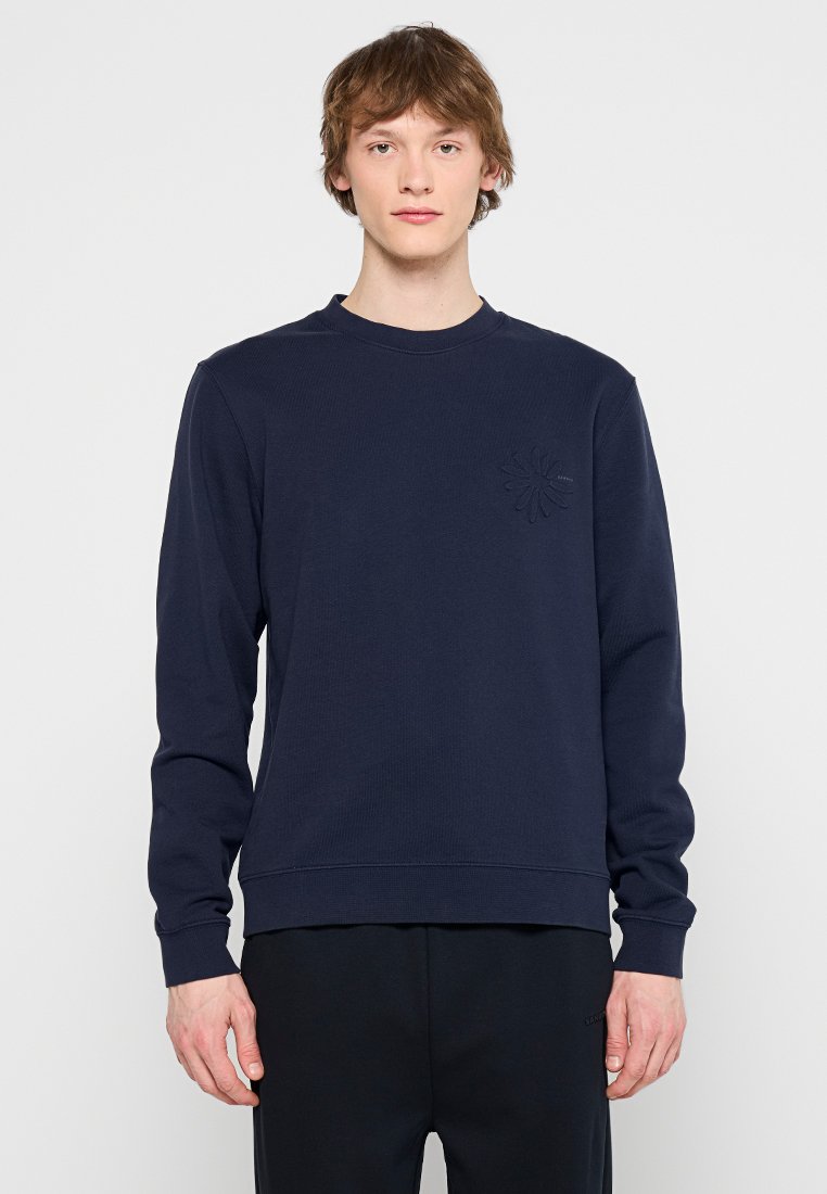Marineblauwe sweatshirt met lange mouwen, ronde hals, gestructureerde stof en een subtiele bloemenlogo-accent op de borst. Ontspannen pasvorm.