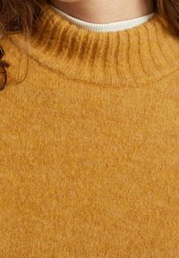 Pull en maille jaune moutarde avec un col rond côtelé et une texture douce, mettant en valeur un tissu lisse et chaud.