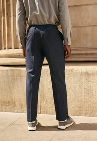 Navy striped trousers with a tapered fit, featuring a flexible waistband, worn with gray sneakers, paired with a light gray long-sleeve shirt.