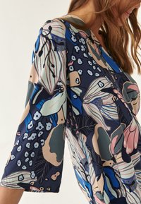 Blusa de estampado floral en azul oscuro, con mangas cortas, escote en V y diferentes tonalidades de rosa, verde azulado y crema, en una tela ligera.