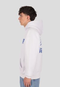 Biela bavlnená mikina s veľkým modrým motívom na prednej strane, nastaviteľnou kapucňou s šnúrkami a bočnými vreckami. Casual strih.