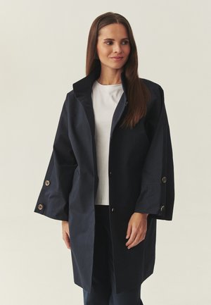 Marineblauer Mantel bis zum Knie mit hohem Kragen, großen Knöpfen an den Ärmeln und minimalistischem Design. Hergestellt aus einem glatten, strapazierfähigen Stoff.