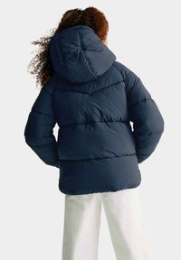 Mörkblå puffjacka med huva, med en quiltad textur och elastiska ärmslut. Synlig sömnad och en avslappnad passform framhäver dess design.