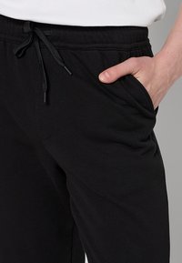 Zwarte trainingsbroek met een trekkoord in de taille, zijzakken en een zachte katoenmix stof; aangesloten boorden bij de enkel.