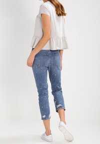 Top peplum gris corto con mangas cortas, combinado con unos jeans azules desgastados que tienen manchas de pintura blanca. Zapatillas blancas completan el atuendo.