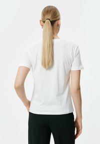 Witte katoenen t-shirt met korte mouwen, een ronde halslijn en een rechte zoom, van de achterkant gezien, gecombineerd met zwarte broeken.