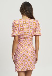 Korte roze jurk met een volledig geometrisch patroon in oranje en wit. Pofmouwen en een getailleerde silhouet met een ritssluiting.
