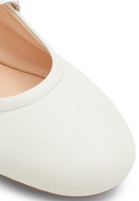 Vit läderplatta med rund tå, slät textur och minimalistisk design. Inredningen har beige foder. Inga märkbara accenter.