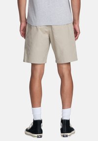 Shorts beiges en tissu léger, avec une coupe décontractée et un ourlet juste au-dessus du genou. Associés à des baskets noires montantes et des chaussettes blanches.