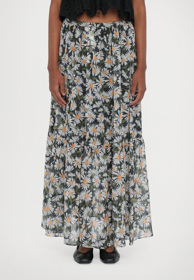 Jupe longue en tissu noir transparent avec un imprimé marguerites blanches au centre orange. Taille élastique et design à volants. Chaussures noires classiques.