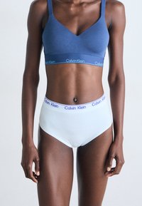 Modrý bralet a bílé kalhotky značky Calvin Klein. Hladký materiál, design ve tvaru V a elastické pásky s logem značky v kontrastních barvách.