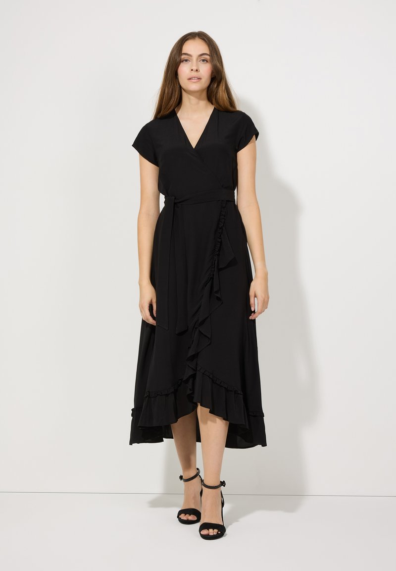 Schwarzes Wickelkleid mit kurzen Ärmeln, versehen mit einem Rüschensaum und einer Bindegurt. Das weiche Material und die fließende Silhouette verleihen dem Design eine besondere Note.