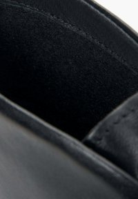 Wnętrze czarnych skórzanych butów z miękką, teksturowaną filcową podszewką. Widoczne przeszywane krawędzie i gładkie wykończenie.