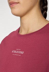 Bordová bavlnená tričko s okrúhlym výstrihom a bielym potlačeným textom "ONLYPLAY ATHLEISURE EST. ACTIVE LIFE 2006" na hrudi.