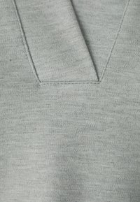 Tela gris claro con un acabado texturizado y un diseño de cuello en V. Detalles de costura visibles alrededor del escote, creando un patrón sutil.