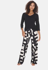 Black v-neck long-sleeve top paired with loose-fitting pants featuring bold black and cream abstract patterns. Soft fabric, relaxed fit.