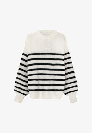 Sweter w paski i wysokie spodnie w paski z sznurkiem, ręka w kieszeni, widoczna metka ubrania SRF nad paskiem spodni.