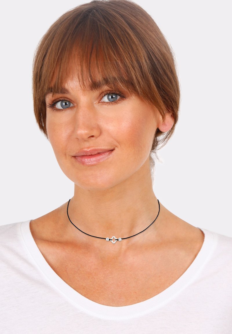 Black choker necklace with silver hardware featuring a central design and two round beads. Worn by a model with shoulder-length hair.