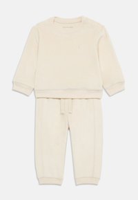 Haut en coton côtelé couleur crème à manches longues avec un col rond et des détails de boutons ; joggeurs assortis avec un cordon de taille et des chevilles côtelées.