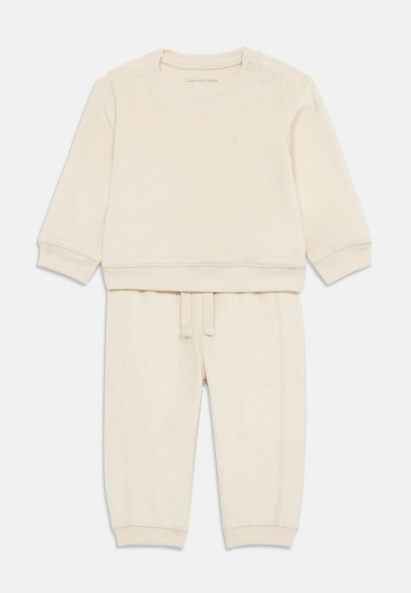 Top a maniche lunghe in cotone a coste color crema con scollatura rotonda e dettaglio con bottoni; pantaloni jogger abbinati con vita con cordino e caviglie a costine.