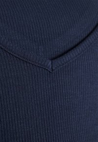 Das dunkelblaue gerippte Material weist ein V-Ausschnitt-Design mit einer glatten Textur und einem subtilen Glanz auf. Die Naht entlang des Ausschnitts ist ordentlich verarbeitet.