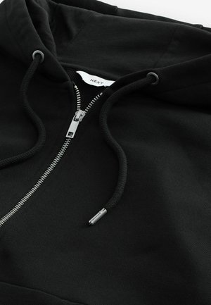 Sudadera negra con cremallera, capucha con cordón, cremallera metálica y tejido texturizado. Presenta una pequeña etiqueta de la marca dentro del cuello.