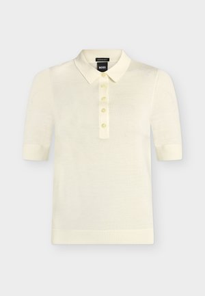Krémové polo tričko s krátkými rukávy, pěti knoflíky, žebrovanými manžetami a spodním lemem a špičatým límcem, štítek značky viditelný uvnitř límce.