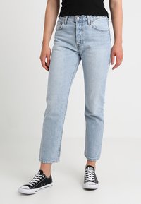 Světle modré džíny s rovný střih, vysokým pasem, pěti kapsami a předním zapínáním na knoflíky, doplněné černými teniskami Converse.