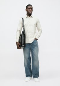 Cămașă bej deschis cu nasturi, blugi albaștri largi, adidași albi și un geantă tote neagră din piele. Design simplu, fără modele vizibile.