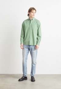 Πράσινο ριγωτό πουκάμισο με κουμπιά φτιαγμένο από ελαφρύ ύφασ�μα, συνδυασμένο με φθαρμένα ανοιχτόχρωμα τζιν και μαύρες μονομάχες. Μινιμαλιστικός σχεδιασμός.