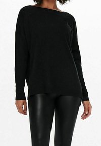Czarny oversize sweter z szerokim dekoltem, długimi rękawami i ściągaczem u dołu. Noszony na czarne leginsy przypominające skórę, ukazujące swobodny fason.