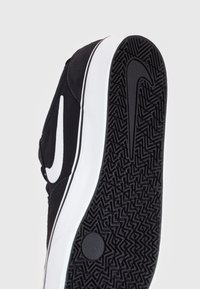 Czarne sneakersy z teksturowaną gumową podeszwą, białym logo Nike, kontrastującą białą podeszwą środkową i zaokrąglonym przodem.