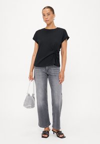 Zwart kortemouwen top met een knoopdetail bij de taille, gecombineerd met hoogwaist, vervaagde grijze jeans en zwarte hoge sandalen.