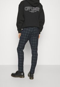 Pantaloni a quadri blu navy realizzati in tessuto leggero, con taglio slim e tasche laterali, abbinati a scarpe in pelle nera e a un hoodie nero.