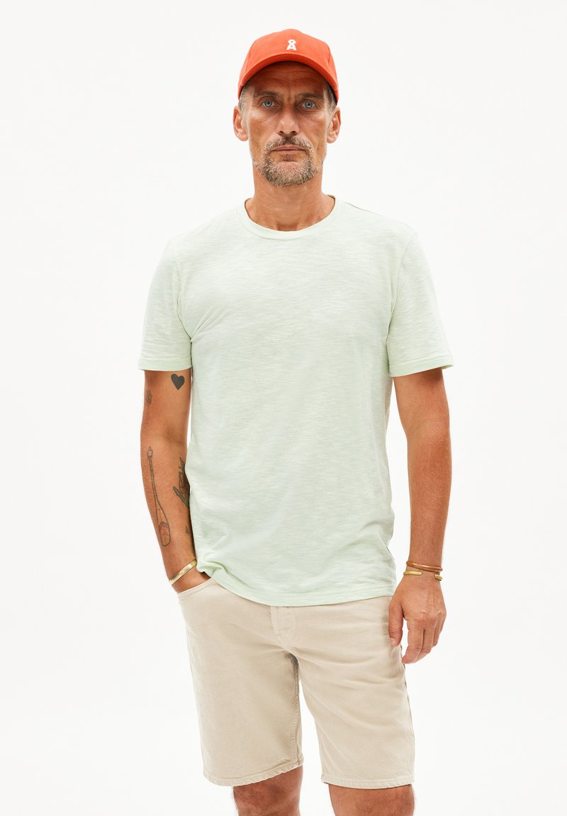 Hellgrünes Kurzarm-T-Shirt mit rundem Halsausschnitt, kombiniert mit beigen Shorts. Der Stoff wirkt weich und hat eine feine Textur.