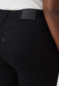 Jeans de mezclilla negra con un bolsillo trasero con un diseño de costura curvada, una etiqueta de marca texturizada y un ajuste slim.