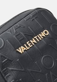 Geantă din piele neagră cu model logo embosat și detalii metalice aurii "VALENTINO". Textură netedă cu o formă structurată.