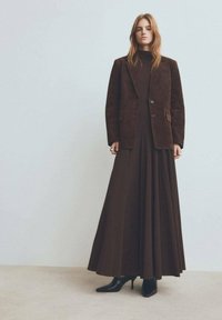 Blazer di corduroy marrone sopra un vestito lungo coordinato. L'insieme presenta una silhouette snella e tacchi a punta nera.