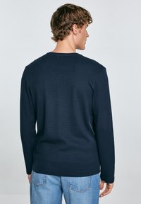 Maglietta a maniche lunghe in navy con collo a girocollo, tessuto testurizzato e taglio dritto, abbinata a jeans azzurri chiari.