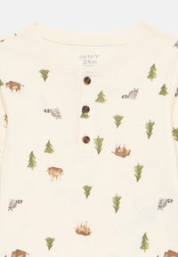 Crèmekleurig katoenen shirt met geborduurde patronen van dieren en bomen, voorzien van drie donkere knopen bij de hals en een zachte textuur.