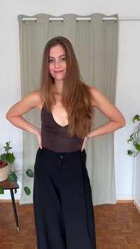 Barna ujjatlan body mély kivágással, magas derekú fekete nadrággal párosítva. Sima anyag és laza szabás. Zöld növények a háttérben.