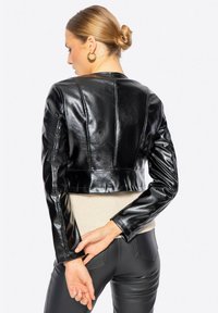 Giubbotto corto in ecopelle nera con finitura lucida, caratterizzato da cuciture strutturate, maniche lunghe e un design aderente sul retro.