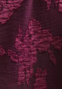 Burgundowa tkanina z teksturowanym, abstrakcyjnym wzorem liści, z postrzępionymi brzegami. Powierzchnia wydaje się miękka i ma subtelny połysk.